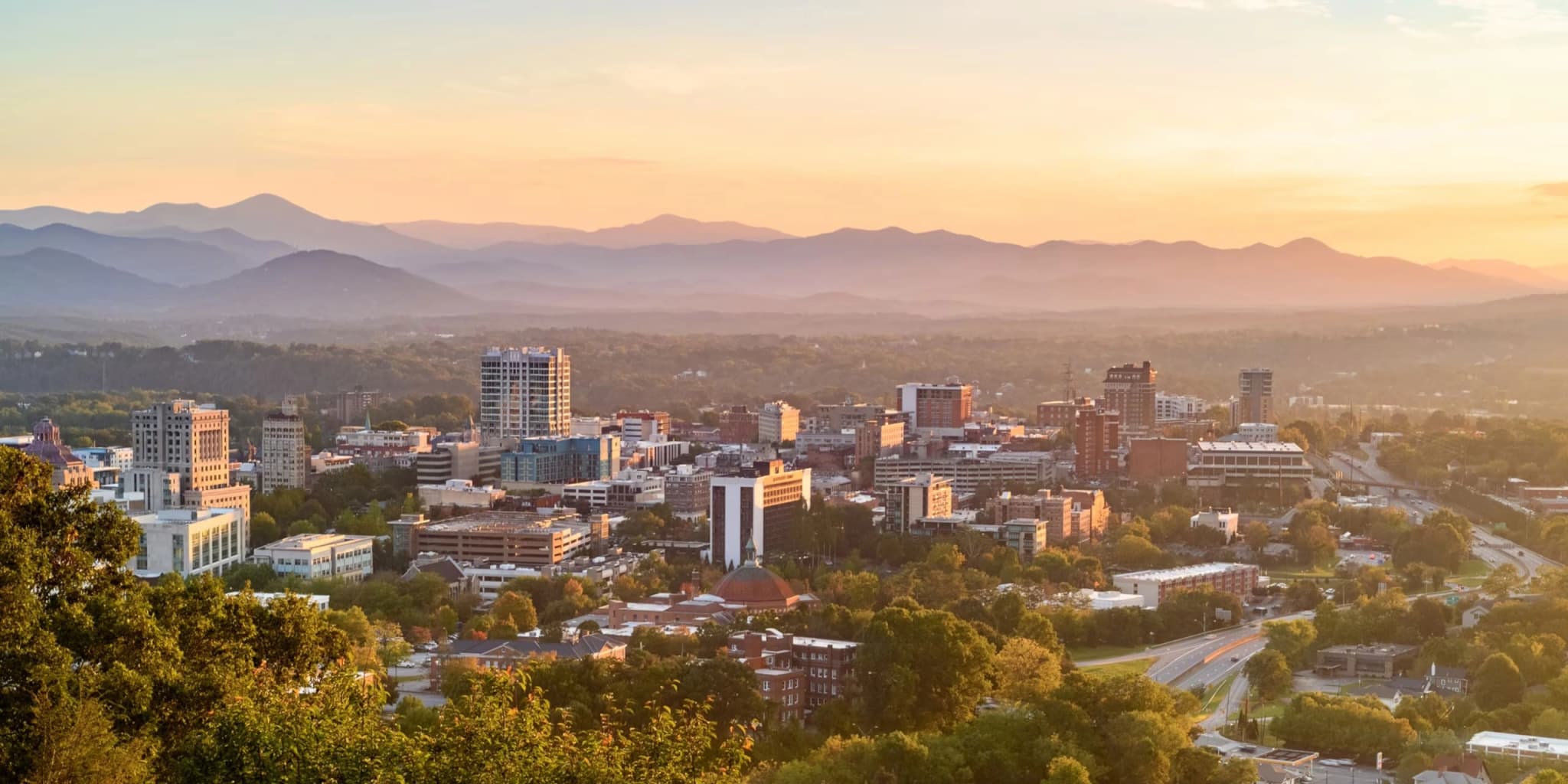Downtown Asheville skyline at sunset with the Blue Ridge Mountains in the background.